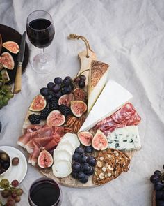 an assortment of cheeses, meats and fruit on a platter with two glasses of wine