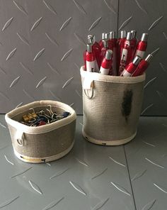 two baskets filled with pens and markers on top of a gray counter next to each other