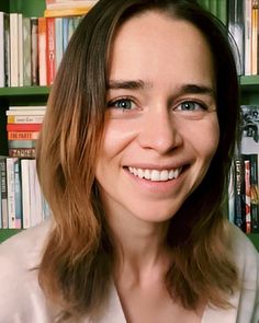 a woman with long hair smiling in front of bookshelves