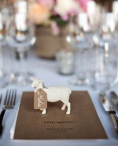 a white sheep figurine sitting on top of a brown menu cover next to silverware