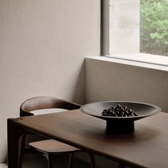 a black plate sitting on top of a wooden table next to a chair and window