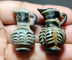 two small black and white vases sitting on top of each other in someone's hand