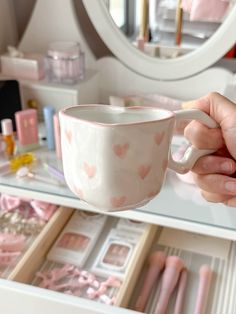 a person holding a coffee cup in front of a vanity with pink accessories on it