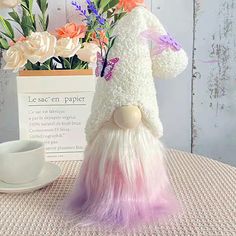 a white and pink stuffed animal sitting on top of a table next to a cup