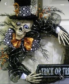 a wreath with a skeleton wearing a top hat and holding a trick or treat sign