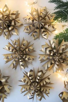 gold paper snowflakes hanging on a white wall with christmas lights around them and pine branches