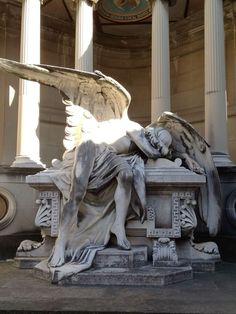 an angel statue sitting on top of a bench in front of a building with columns