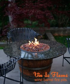 a fire pit sitting on top of a wooden barrel next to two chairs and a table