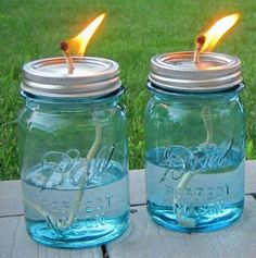 two mason jars with candles in them sitting on a wooden table next to some grass