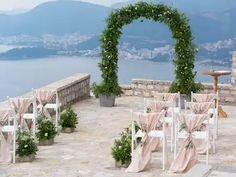 an outdoor ceremony set up with white chairs and pink sashes, overlooking the water