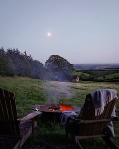 two wooden chairs sitting on top of a grass covered field next to a fire pit