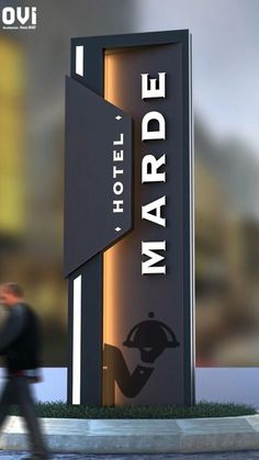 a man walking past a hotel sign in front of a blurry image of a building