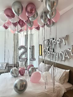 balloons and streamers are hanging from the ceiling above a bed in a room with white walls