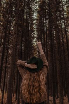 a woman standing in the middle of a forest with her hands up to her head