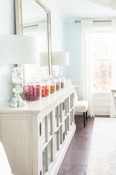 a living room filled with furniture and a large mirror on top of a dresser next to a window