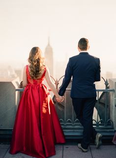 a man in a suit and woman in a red dress holding hands on a balcony