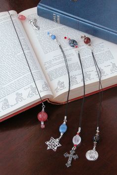 an open book on a table next to several necklaces and a cross pendant in front of it