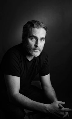 a black and white photo of a man with a beard sitting in front of a window