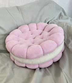 a pink and white round cushion on top of a gray bed spread with grey sheets