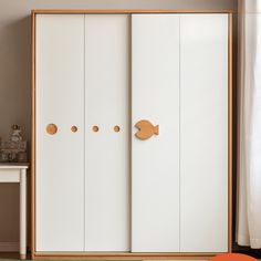 a white closet with three doors and two knobs on the front, next to a small table