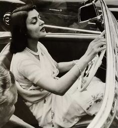 an old photo of a woman sitting in the driver's seat of a car