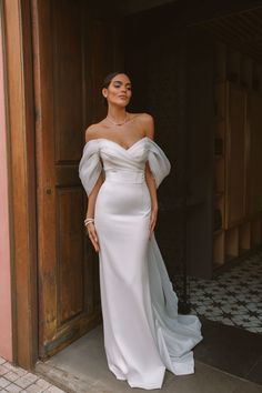 a woman standing in front of a door wearing a white dress with sleeves on it