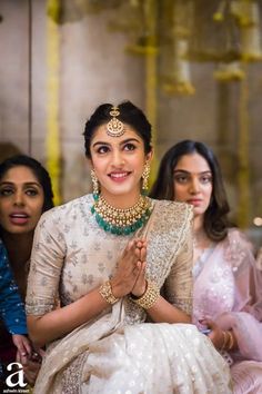 a woman sitting in front of two other women with jewelry on her neck and hands clasped