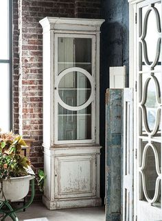 an old white china cabinet sitting next to a potted plant in front of a window