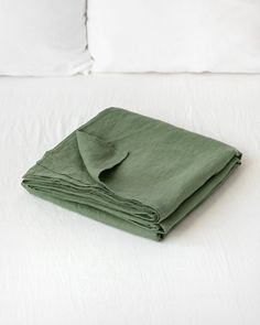 a folded green blanket on top of a white bed