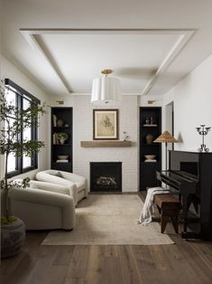 a living room filled with furniture and a piano in front of a fire place on top of a hard wood floor