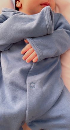 a baby laying on top of a bed wearing a blue outfit