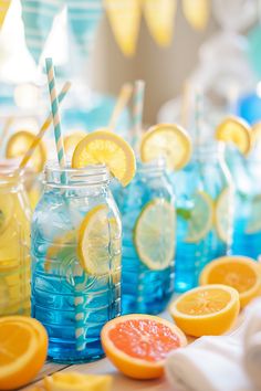 several mason jars filled with lemons, oranges and blue water are lined up on a table