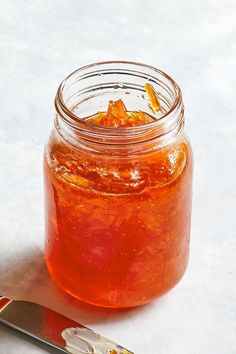 a glass jar filled with orange peels next to a knife on a white surface