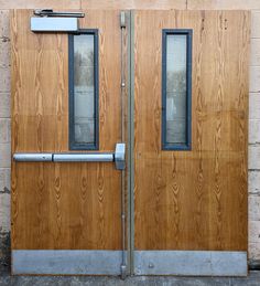 two wooden doors with metal handles and bars on each side, against a brick wall