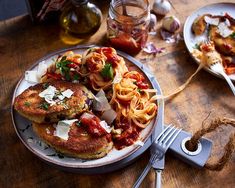 two crab cakes with pasta and sauce on a plate next to a knife and fork