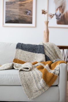 a white couch with a blanket on top of it next to a vase filled with flowers