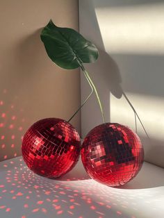 two red disco ball vases sitting on top of a white table next to a green leaf