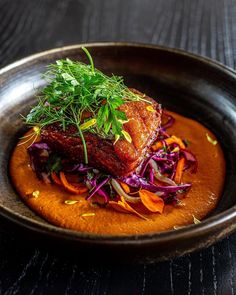 a plate with some meat and vegetables in it on a wooden table next to a fork