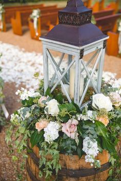 a candle is lit on top of a wooden barrel with flowers and greenery in it