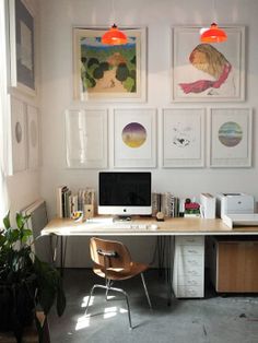 a desk with a computer on top of it in front of pictures and potted plants