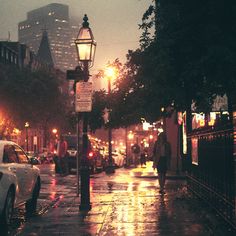 a city street at night with cars parked on the side walk and people walking down the sidewalk