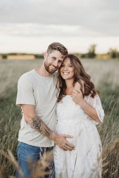 a man and woman standing in tall grass smiling at the camera with their arms around each other