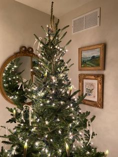 a small christmas tree with white lights in a living room next to a mirror and framed pictures on the wall