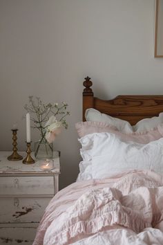 a bed with white sheets and pink comforter next to a small table with flowers on it