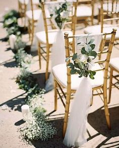 the chairs are lined up with white flowers and greenery for an outdoor wedding ceremony