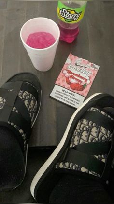 someone's feet with their shoes on, next to a cup of pink liquid