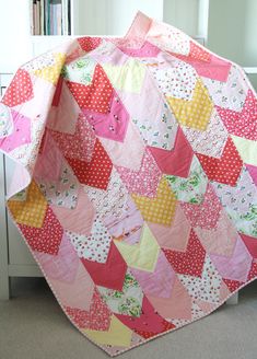 a pink and yellow patchwork quilt sitting on top of a white dresser next to a window