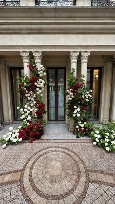 an entrance to a building with flowers growing on the columns and around it is a circular mosaic tile floor