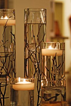 candles in glass vases with twig stems and branches on the side, sitting next to each other