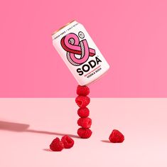 a can of soda with raspberries falling off the side on a pink background